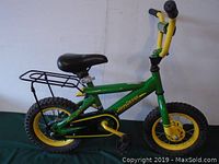 Side profile of John Deere small children's bike showcasing green frame, black seat, and yellow accents including wheels and pedals.