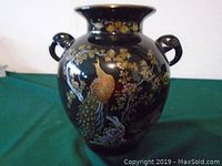 Front view of the vase showing detailed colorful peacock and flowers on a black background.
