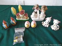 Several pairs of assorted ceramic collectible salt and pepper shakers on a green cloth background, including corn, cats, roosters, ducks, and eggs.