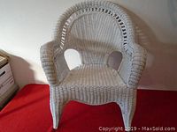 Front view of the white painted wicker chair showing the woven seat, armrests, and rounded backrest with symmetrical openings beneath the arms.