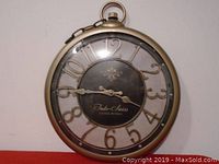 Front view of Indo-Swiss round wall clock with gold-tone frame and black center showing hands and raised gold numbers.