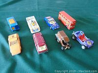 Eight die-cast toy cars and trucks arranged on a green surface in a single photo revealing the variety of models and colors.