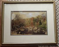 Framed painted photograph showing a landscape with river, stone bridge, rocks, and trees in a decorative frame.