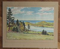 Frontal view of the matted watercolour painting depicting a landscape scene with trees, hills, and water under a blue cloudy sky. Shows good overall presentation with visible signature and matte board framing.