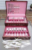 Full view of two wooden boxes lined with pink fabric containing multiple rows of silverplate knives, forks, and spoons neatly arranged with some loose pieces.