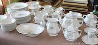 Photo of the full 88 piece set arranged on table showing plates stacked in piles, cups and saucers, teapots, serving dishes and other accessories.