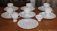 Full view of 6 complete place settings each with cup, saucer, and plate, showing floral pattern and pink interiors of cups.