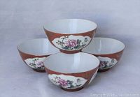 Four vintage Chinese porcelain cups arranged with one balanced on top of three. Cups have a reddish-brown background with white oval panels featuring pink floral designs.