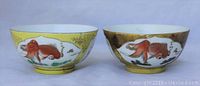 Front view of two vintage Asian porcelain cups featuring colorful goldfish on yellow and brown backgrounds with gold accents.