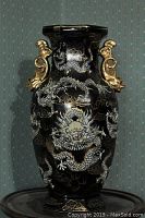 Front view of large black pottery vase with white enamel dragon and gold gilt detail on raised designs, plus gold gilt sculpted handles.