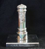 Front view of the small silver fountain figurine showing the inscription on the base and decorative top.