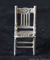 Front view of miniature sterling silver chair showing detailed backrest and seat.