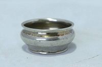 Photo showing side view of a small round sterling silver salt cellar with a flared lip and marks of age-related tarnish and wear.