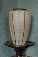 Front view of large striped mid-century vase on wooden stand, showing vertical stripes in brown, yellow, and blue on cream background