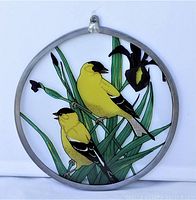 Close front view of first round stained glass panel showing two yellow birds perched on green leaves and purple iris flowers.