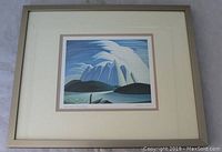 Framed print showing full artwork with landscape of blue mountains, lake, and sky. Wooden frame and matting visible.