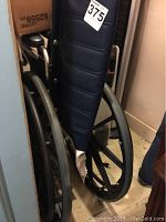 Manual wheelchair showing padded backrest, metal frame, and large rear wheels with hand rims for self-propulsion.