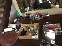 Two computer speakers, calculator alarm clock, toy trucks, collectibles and packaged items shown on couch and in box