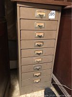 Front view of metal file cabinet with 9 drawers, showing wear and label holders on drawers.