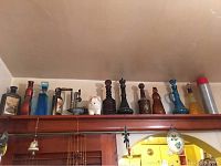 Wide shot showing all vintage bottles, meat grinder, thermos, and pig figurine on top shelf above cabinetry.