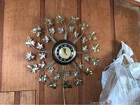 Full view of the mid century electro wall clock mounted on wood panel with metal decorative leaf stems radiating from the center clock face.