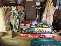 Wide shot of lot contents showing various boxed vintage games and electronic items stacked on table and shelf