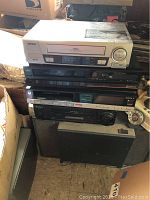 Stack of VHS and Betamax VCR devices with a speaker and a telephone visible