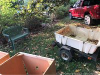 Overall view showing the green vinyl bench and the white plastic car carrier mounted on the black metal trailer frame with a red truck partially visible in the background.