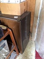 Photo showing side angle of the mini fridge with wood-grain laminate exterior and black trims. Shows power cord on side and overall compact design.