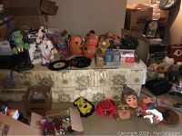 Photo showing assorted vintage Halloween masks on the floor and on table, various other items like plastic cups and boxes visible