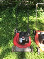 Full view of the red and black Briggs and Stratton lawn mower outdoors on grass with handle upright.
