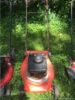 Full view of red Hechinger 21 inch lawn mower with push handle placed outdoors on green plants.