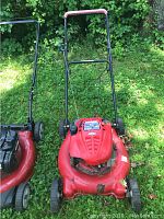 Photo of the full red Troy Bilt lawn mower with black handle, showing the deck, wheels, and handlebar in a grassy outdoor setting.