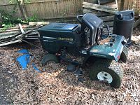 Green Craftsman riding mower seen from side outside with dirt and leaf debris on deck and tires.