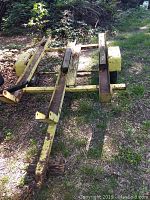 Side angle of yellow motorcycle trailer frame showing metal rails, single axle, and rusted condition.
