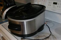 Side view of the Kitchen Aid slow cooker showing stainless steel body, black handles, and glass lid.