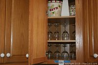 Wooden cabinet shelf showing eight clear stemmed wine glasses arranged in two rows.