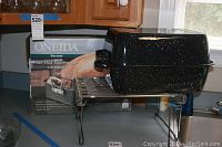 Oneida black speckled non-stick roasting pan on metal V-rack with handle visible and box in background