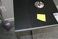 Black TV tray with metallic legs next to a Shark upright vacuum cleaner in a corner of a carpeted room.
