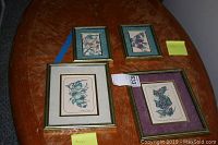 Four framed botanical prints on a wooden table, two larger 9x11 and two smaller 8x6 prints arranged with sticky notes for size indication.