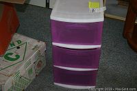 Front view of white frame storage unit with three purple drawers placed on carpeted floor.