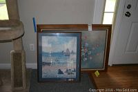 Two framed artworks leaning against a wall near a door, showing a beach scene and floral painting.