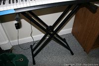 Close-up photo showing the lower part of the keyboard and the black X-style metal stand supporting it.