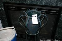 Tall metal flower stand with blue-green finish photographed in front of a fireplace.
