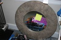 Large round carved wooden framed mirror with a blue basket in front containing hair styling tools.