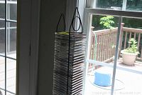 Tall black metal CD stand filled with assorted CDs in jewel cases viewed near a window.