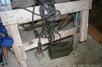 Two wooden saw horses with a drop cord wrapped around one, showing the protective cage for the bulb and attached cable.
