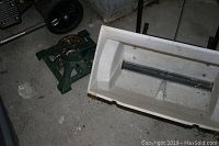 Photo of the green cast iron tree stand next to the white plastic drop spreader on a concrete floor.