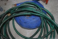 Close-up of coiled green and blue water hoses on concrete floor.