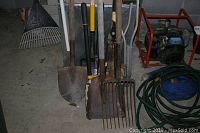 Various yard tools including rake, shovels, pitchfork, pruning clippers and part of generator and hose in background